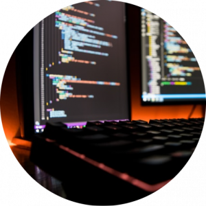 Developer workstation with code on dual monitors representing the Build Zone of the SoT AI Enterprise Reference Model -- where AI development, applications, and automation are built and deployed